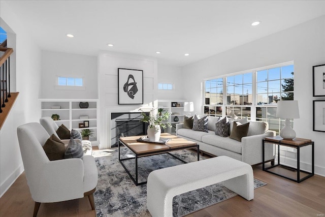 living room with a glass covered fireplace, a healthy amount of sunlight, stairway, and wood finished floors