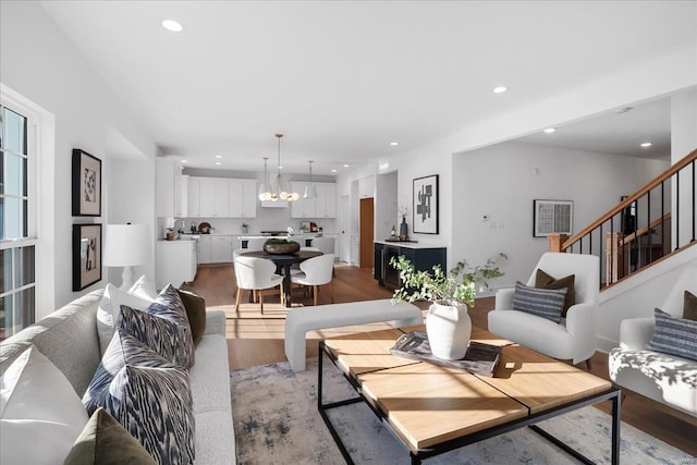 living area featuring light wood-type flooring, recessed lighting, an inviting chandelier, and stairs