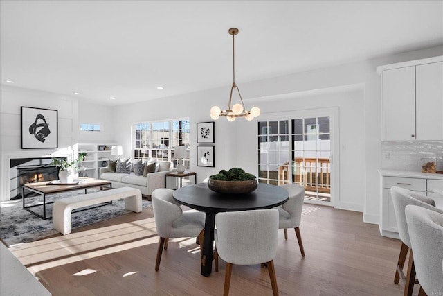 dining space featuring recessed lighting, a notable chandelier, wood finished floors, and a glass covered fireplace