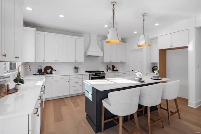 kitchen with gas stove, white cabinets, a sink, and custom exhaust hood