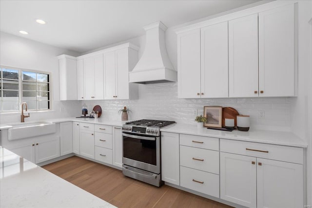 kitchen with a sink, light countertops, gas stove, and custom exhaust hood