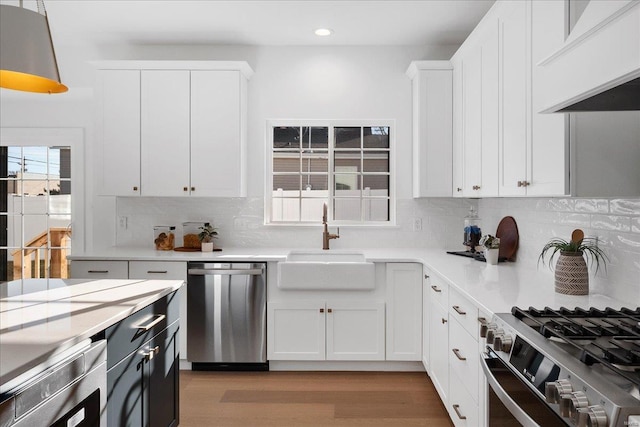 kitchen featuring light countertops, appliances with stainless steel finishes, white cabinets, a sink, and premium range hood