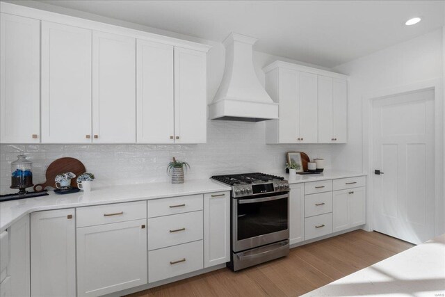 kitchen with light wood-style floors, gas stove, white cabinets, and custom range hood