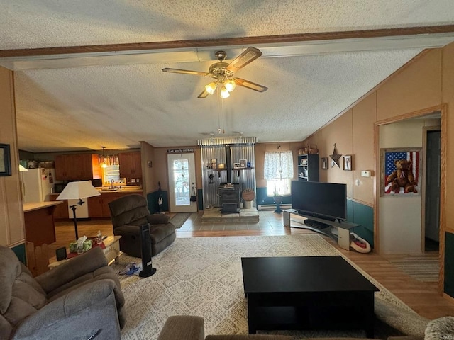 living area with vaulted ceiling, a textured ceiling, a wood stove, and a ceiling fan