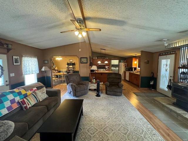 living room with arched walkways, a wood stove, vaulted ceiling, a textured ceiling, and light wood-style floors