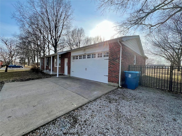 view of side of home featuring driveway, brick siding, an attached garage, and fence