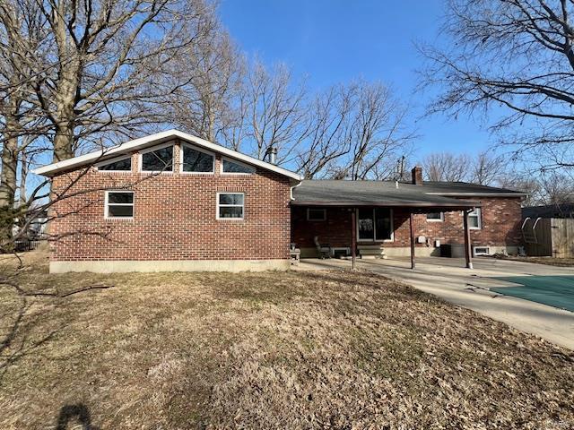 rear view of property with driveway, brick siding, a chimney, and an attached carport