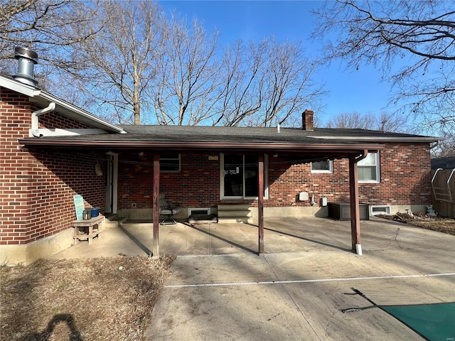 rear view of house with brick siding, a chimney, and a patio area