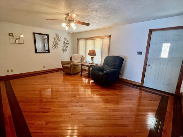 sitting room featuring baseboards, ceiling fan, a textured ceiling, and light wood finished floors