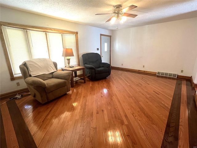 living area featuring baseboards, visible vents, a textured ceiling, and light wood finished floors