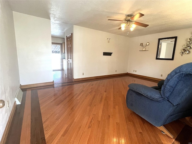 sitting room featuring a ceiling fan, a textured ceiling, baseboards, and wood finished floors