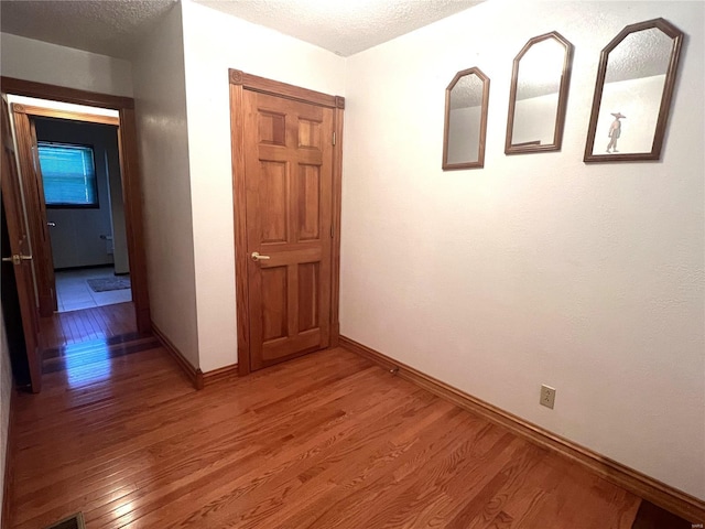 corridor with a textured ceiling, light wood-style flooring, and baseboards