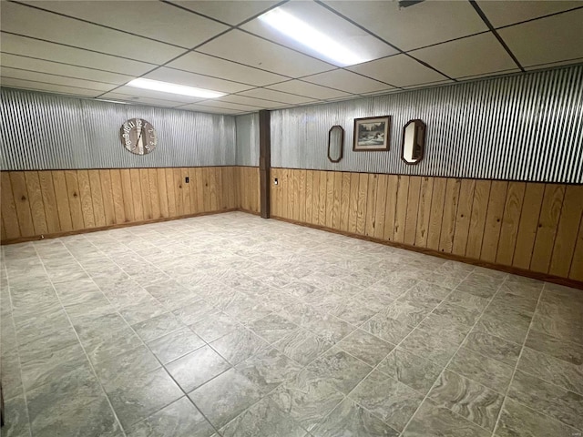 finished basement with wood walls, a drop ceiling, and tile patterned floors