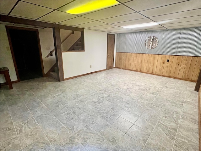 finished basement with wainscoting, wood walls, a drop ceiling, baseboards, and stairs