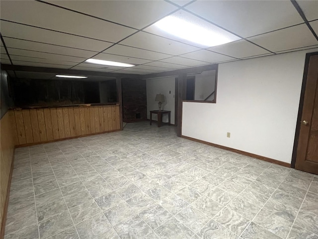 finished basement featuring light floors, a drop ceiling, wooden walls, and baseboards