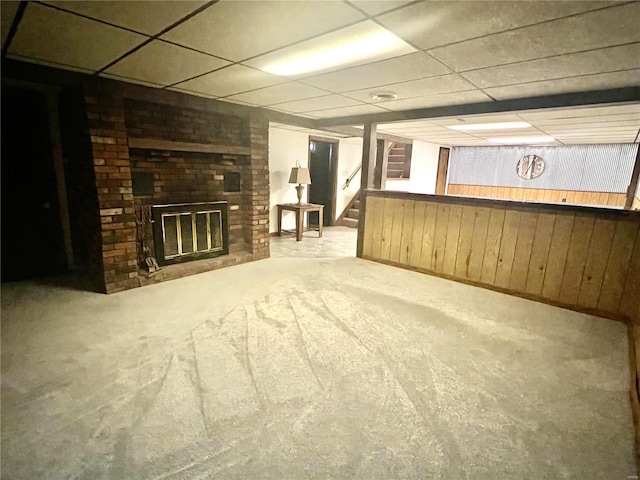 unfurnished living room with wooden walls, a drop ceiling, stairway, carpet, and a fireplace