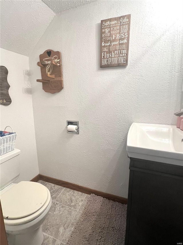 bathroom featuring toilet, vaulted ceiling, vanity, a textured ceiling, and baseboards