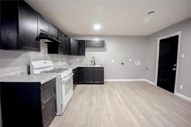 kitchen featuring light wood-style flooring, a sink, white range with gas stovetop, under cabinet range hood, and baseboards