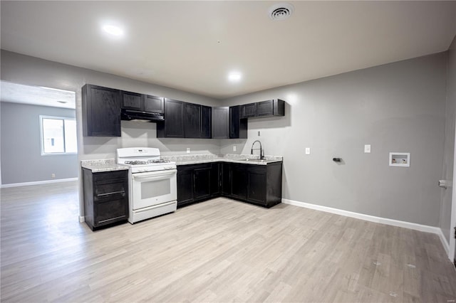 kitchen featuring white range with gas cooktop, visible vents, dark cabinets, light wood-style floors, and exhaust hood