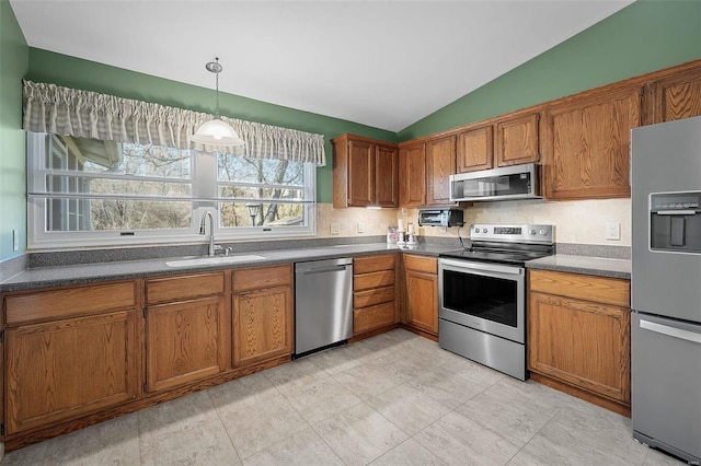 kitchen with a sink, vaulted ceiling, brown cabinetry, and stainless steel appliances