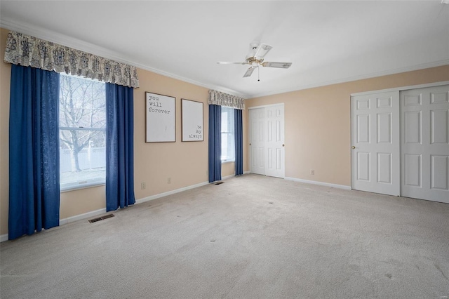 unfurnished bedroom featuring carpet, baseboards, visible vents, ornamental molding, and multiple closets