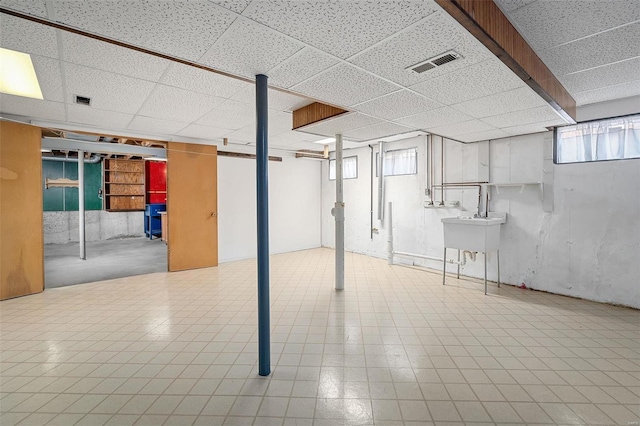 basement featuring a paneled ceiling, visible vents, and a sink