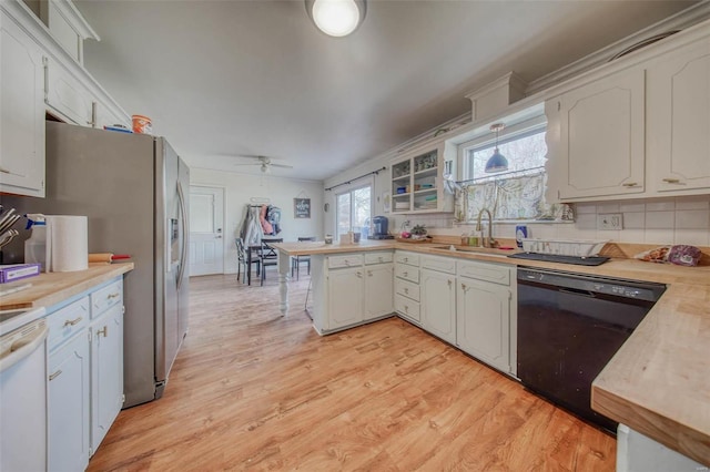 kitchen with light wood finished floors, a sink, black dishwasher, a peninsula, and light countertops