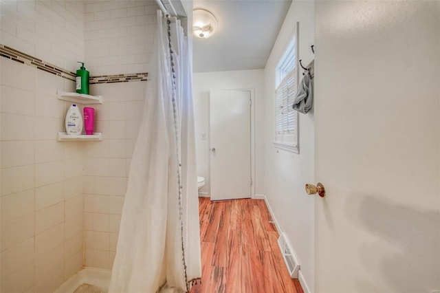 full bathroom with visible vents, toilet, wood finished floors, baseboards, and tiled shower