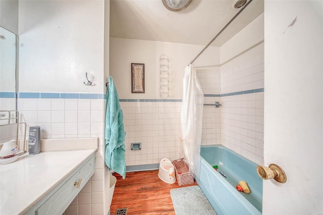 bathroom featuring visible vents, a wainscoted wall, wood finished floors, tile walls, and shower / bathtub combination with curtain