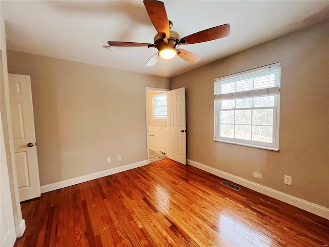 spare room featuring a ceiling fan, visible vents, baseboards, and wood finished floors