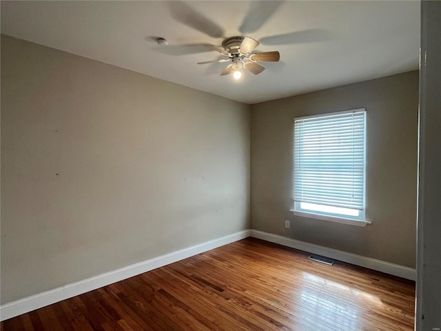 unfurnished room with a ceiling fan, wood finished floors, visible vents, and baseboards