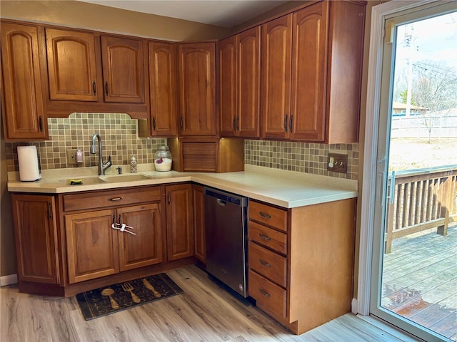 kitchen featuring light wood finished floors, light countertops, stainless steel dishwasher, and a sink