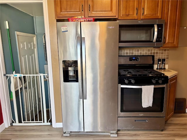 kitchen with appliances with stainless steel finishes, brown cabinets, light wood finished floors, and tasteful backsplash