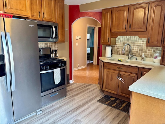 kitchen with arched walkways, stainless steel appliances, a sink, light countertops, and brown cabinetry