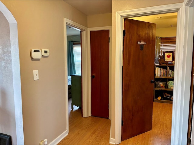 hall featuring arched walkways, baseboards, and light wood finished floors