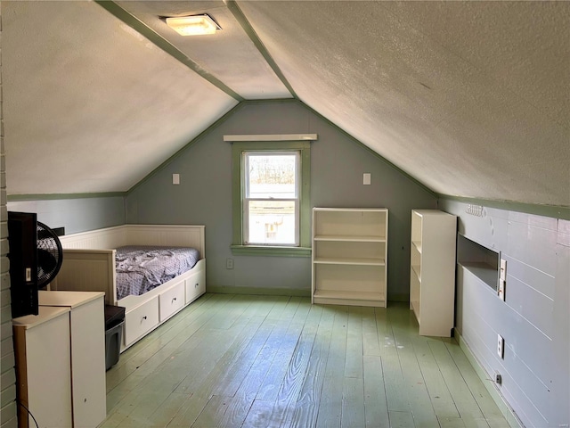 unfurnished bedroom with lofted ceiling, a textured ceiling, and hardwood / wood-style flooring