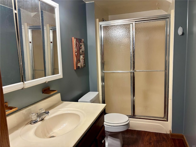 bathroom featuring wood finished floors, a shower stall, toilet, and vanity