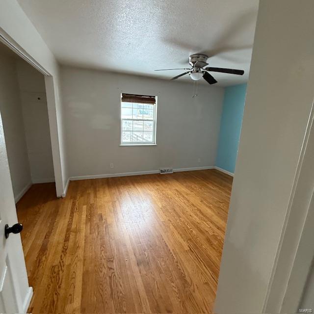 unfurnished bedroom featuring a textured ceiling, ceiling fan, light wood-style flooring, and baseboards