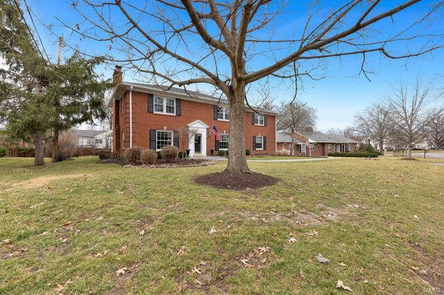 colonial-style house featuring a front yard, brick siding, and a chimney