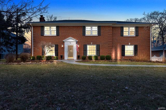 colonial inspired home with a front yard, brick siding, and a chimney