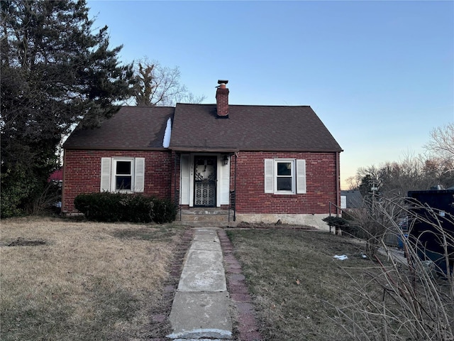 view of front facade featuring roof with shingles, brick siding, a chimney, and a front lawn