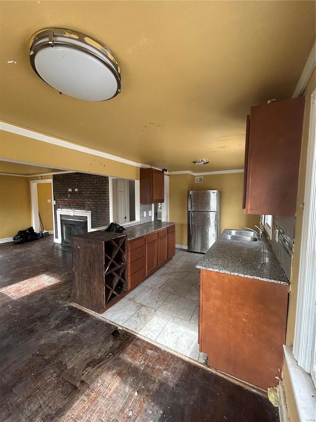 kitchen with a fireplace, a sink, ornamental molding, freestanding refrigerator, and brown cabinetry