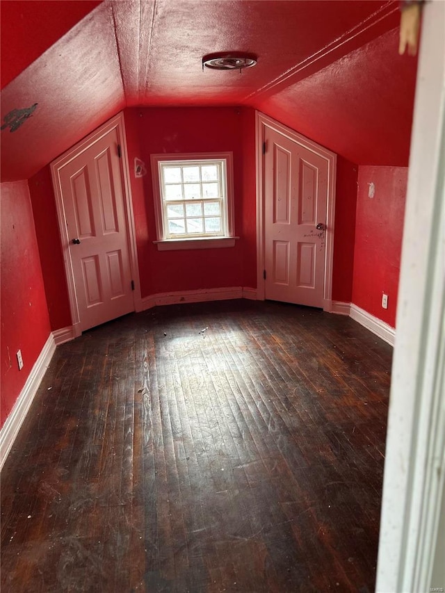 bonus room featuring lofted ceiling, hardwood / wood-style flooring, baseboards, and a textured ceiling