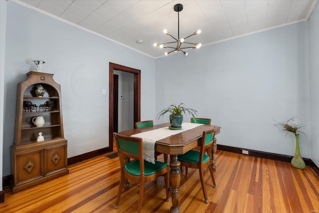 dining space featuring light wood-type flooring, crown molding, baseboards, and an inviting chandelier