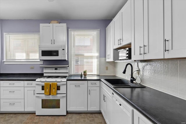 kitchen featuring tasteful backsplash, dark countertops, white cabinets, a sink, and white appliances