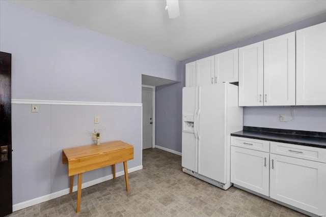 kitchen with dark countertops, white fridge with ice dispenser, baseboards, and white cabinets