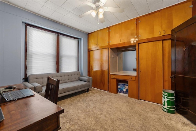 office with carpet floors, wood walls, and ceiling fan