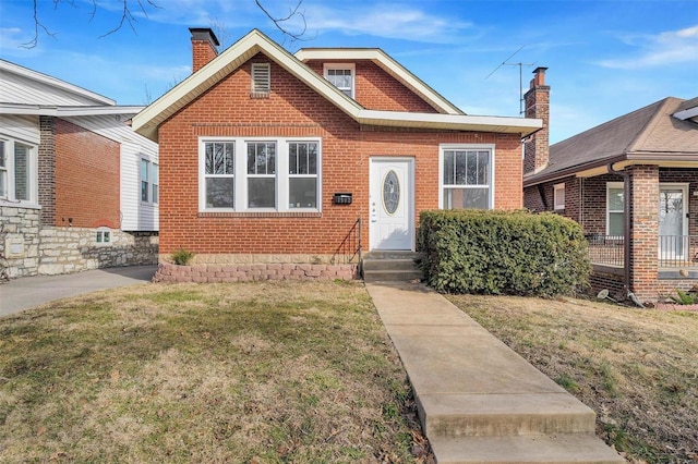 bungalow-style house with a chimney, a front lawn, and brick siding