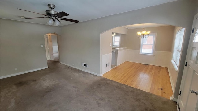 unfurnished room featuring a ceiling fan, arched walkways, a wainscoted wall, and visible vents