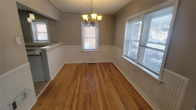 unfurnished dining area with plenty of natural light, light wood-type flooring, wainscoting, and a notable chandelier